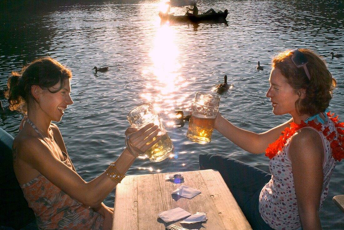 Junge Frauen stoßen mit Bier an, Biergarten Seehaus, Englischer Garten, München, Bayern, Deutschland