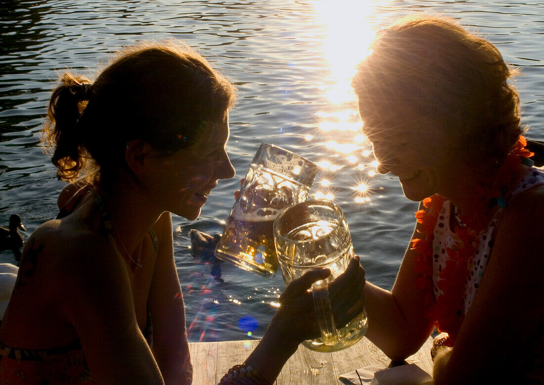 Junge Frauen stoßen mit Bier an, Biergarten Seehaus, Englischer Garten, München, Bayern, Deutschland