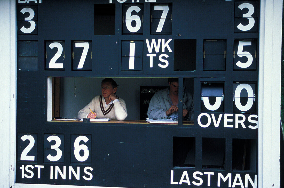 Menschen sitzen hinter einer Anzeigetafel, Village Cricket, Tonbridge, Kent, England Großbritannien, Europa