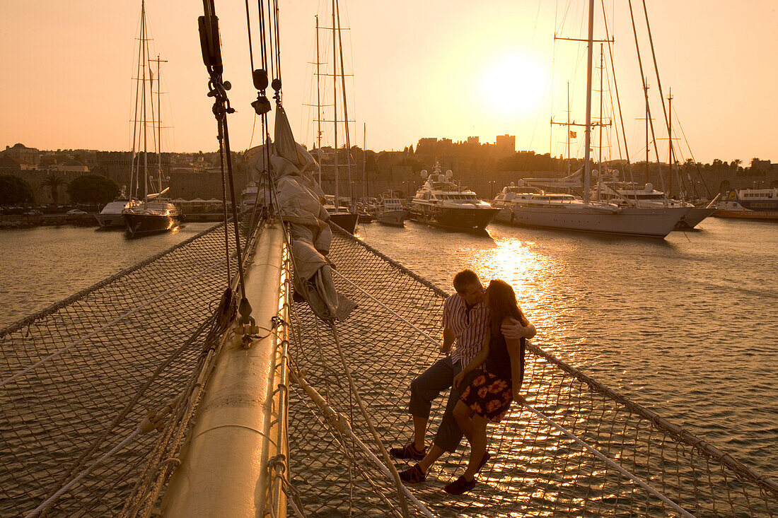 Couple in Bowsprit Net, Star Flyer, sunset over the Rhodes Harbor, Rhodes, Dodecanese Islands, Greece