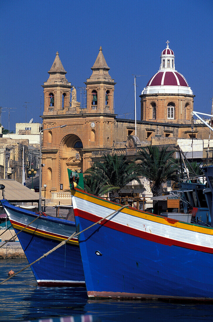 View of fishing boats at harbour and church, Marsaxlokk, Malta, Europe