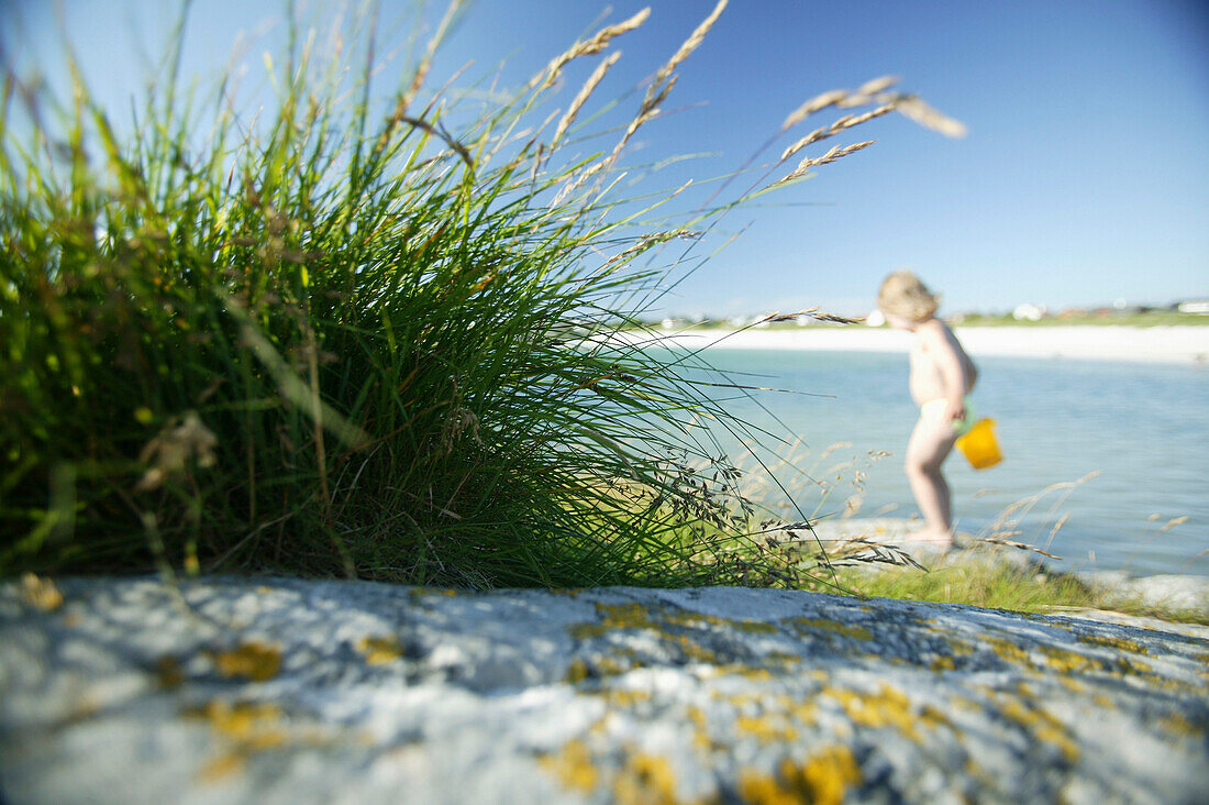 Child on the beach carrying a bucket, Akrasanden, Karmoy Island, Rogaland, Norway