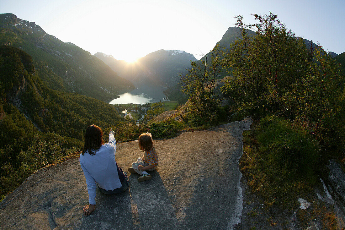 Mother with daughter sitting on rocks above Geiranger Fjord, Romsdal, Norway
