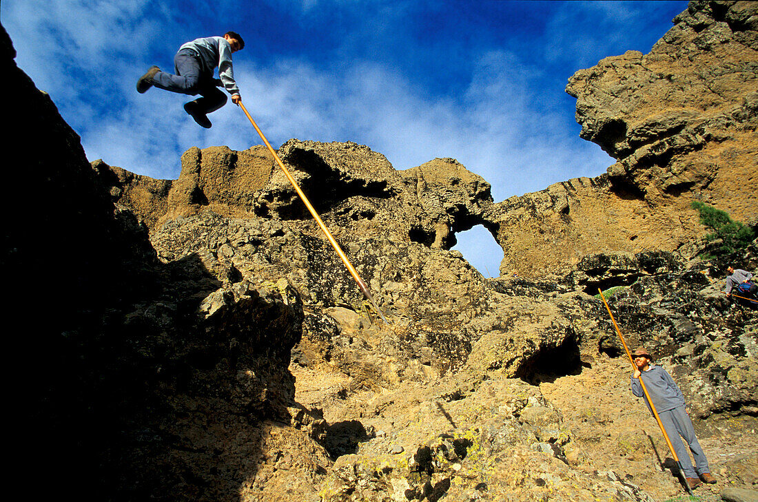 Man leeping over rocks with a Canarian shepherd stick, Gran Canaria, Canary Islands, Spain