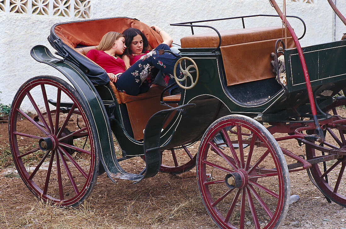 Zwei junge Frauen rasten in einer Kutsche, Romeria de San Isidro, Nerja, Costa del Sol, Provinz Malaga, Andalusien, Spanien, Europa