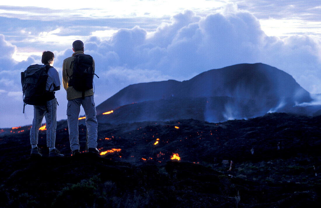 Two people watching glowing lava at Piton Kapor volcano, Ille de la Réunion, Indian Ocean