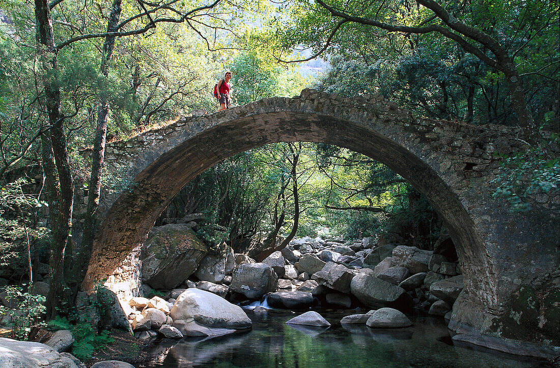 Woman hiking on old bridge, Pont de Zaglia, Spelunca Canyon, Corsica, France