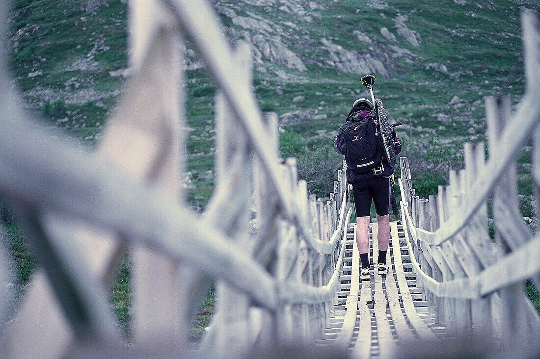 Mann trägt sein Mountainbike über eine Hängebrücke, Norwegen