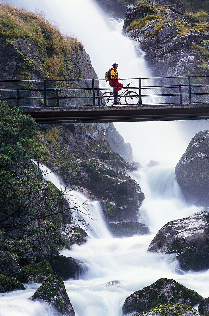 Fahrradfahrer bei Kleivafossen Wasserfall, Briksdal Gletscher, Norwegen