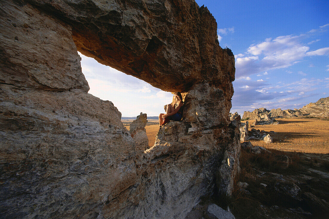 Woman sitting on a rock formation, La Fenetre, Isalo National Park, West Madagascar, Africa