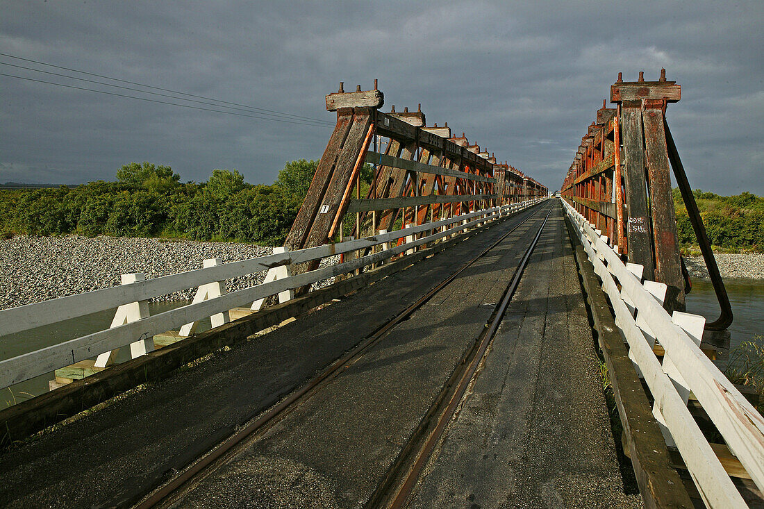 Holzbrücke unter Wolkenhimmel, Eisenbahn und Strassenverkehr teilen sich die schmale Brücke, Westküste, Südinsel, Neuseeland, Ozeanien