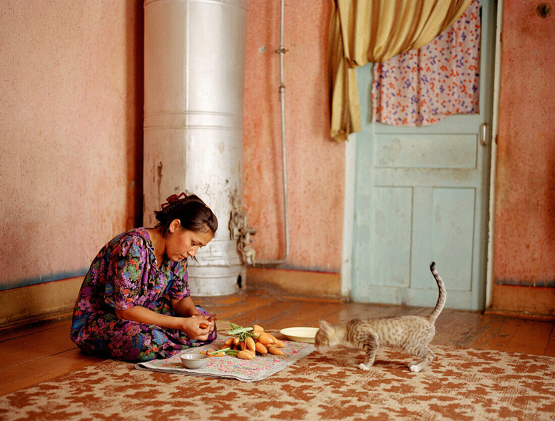 Woman cutting vegetables in front of curious cat, Uzbekistan