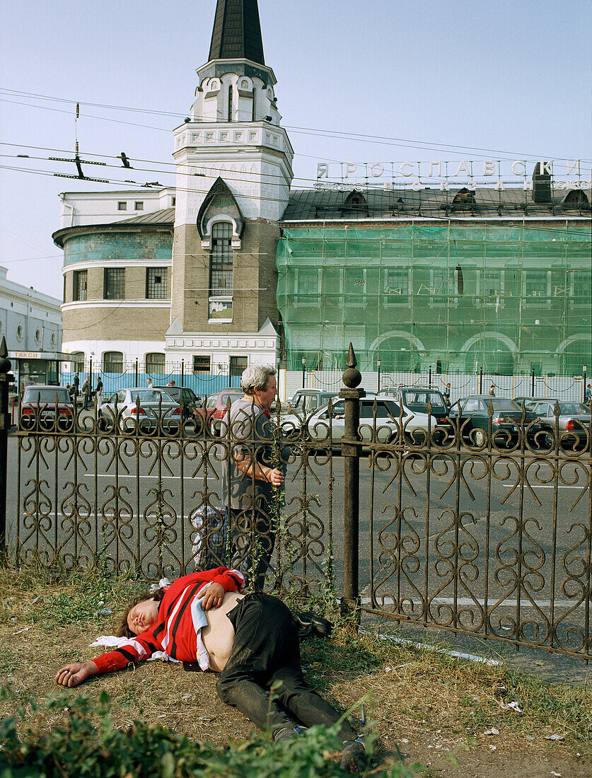 Ein Mann liegt auf dem Boden, im Hintergrund der Yaroslaw Bahnhof, Moskau, Russland