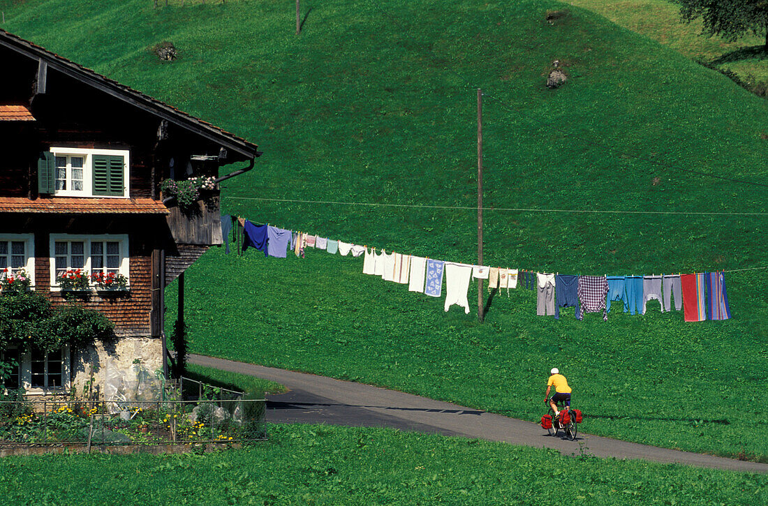 Fahrradfahrer fährt an einem Bauernhaus mit einer Wäscheleine vorbei, Hinterthal, Muotathal, Schwyz, Schweiz