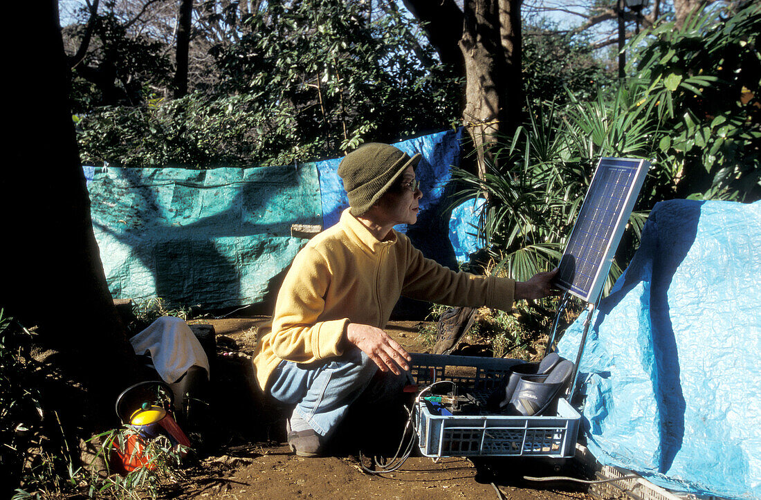 Homeless, living boxes in Tokyo, Japan, Homeless community in Ueno Park woman checking her solar panel for electricity of her tiny TV in a basic tent Obdachlose, notduerftige Schutzbauten, Pappkarton-Architektur, Plastikplanen, Slum, Obdachlosigkeit, Rand