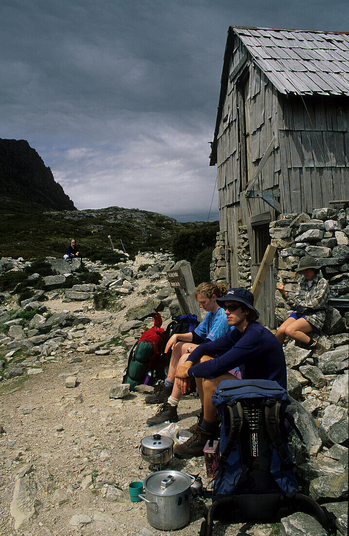 Wanderer mit Campingherd sitzen vor der Kitchen Hut, am Bergfuß Cradle Mountain, Overland Track, Cradle-Mountain-Lake-St.-Clair-Nationalpark, Tasmanien, Australien