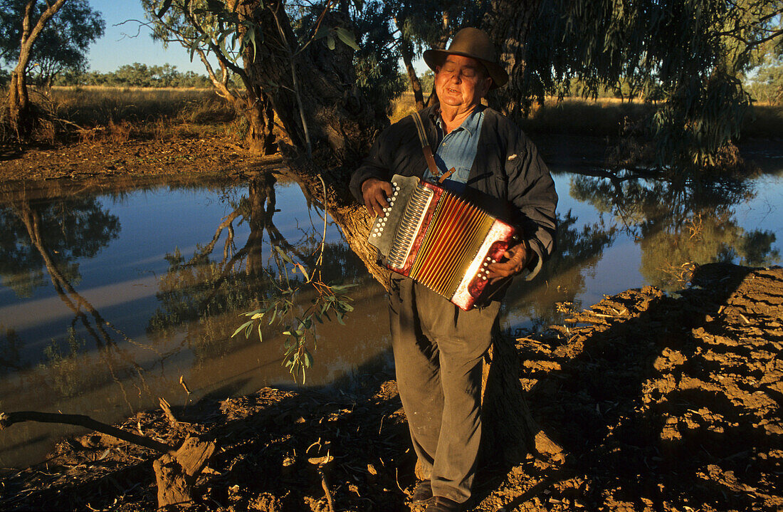 Richard Magoffin, Kynuna, Matilda Highway, Australien, Qld, Matilda Hwy, Richard Magoffin, Historiker spielt Waltzing Matilda neben einem Wasserloch bei Kynuna Australia's National-Lied, Richard Magoffin local historian plays Waltzing Matilda on the banks