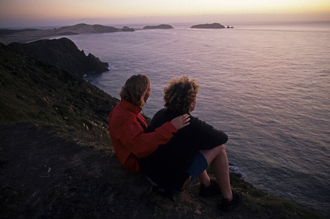 Paar betrachtet Sonnenuntergang am Cape Reinga Kap, dem nördlichsten Punkt Neuseelands, Nordinsel, Neuseeland