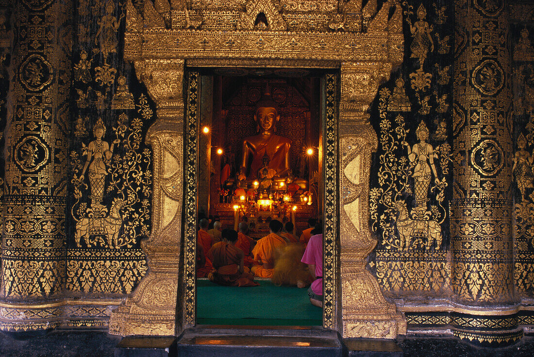 Mönche sitzen bei Kerzenlicht vor einer Buddhastatue, Tempel Wat Xieng Thong, Luang Prabang, Laos, Asien