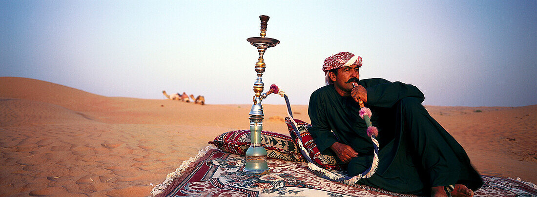 Bedouin smoking waterpipe in the desert, Dubai, United Arab Emirates