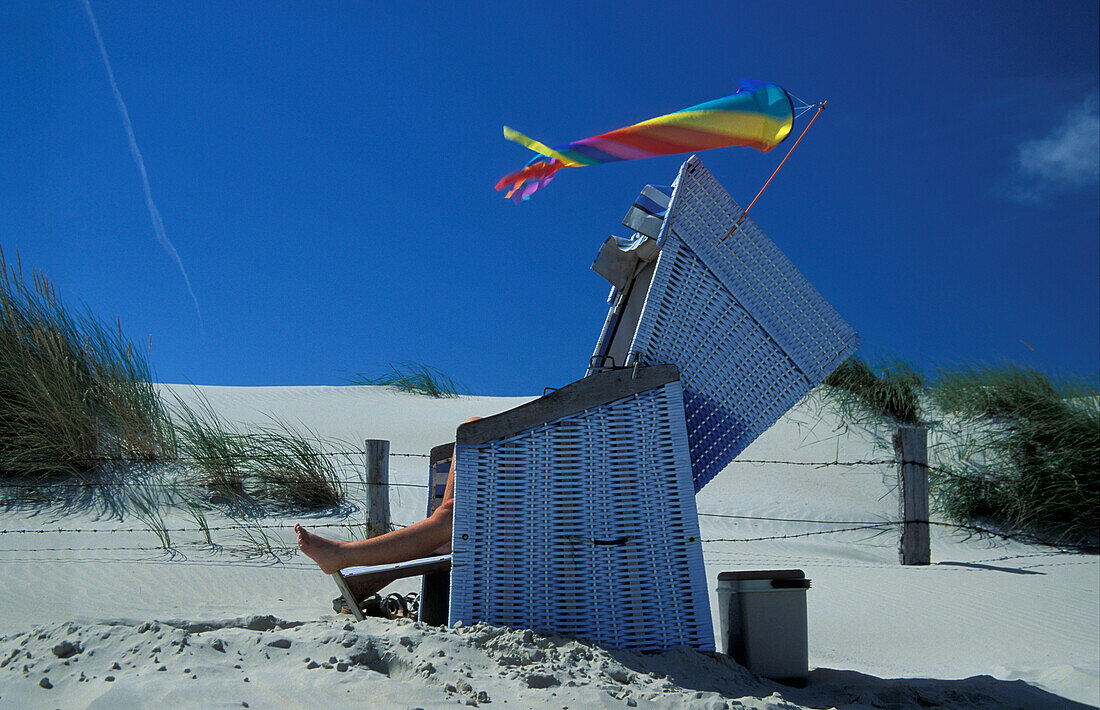 Person lying on beach chair, Island Norderney, North Sea, Islands of Eastern Frisia, Island Norderney, One Person, Mid Adult Women, Leg, Lying, Sunbathing, Relaxing, Beach Chair, Beach, Sand, Clear Sky, Sand Dunes, Grass, Wind Chime, Wind, Side View, Holi