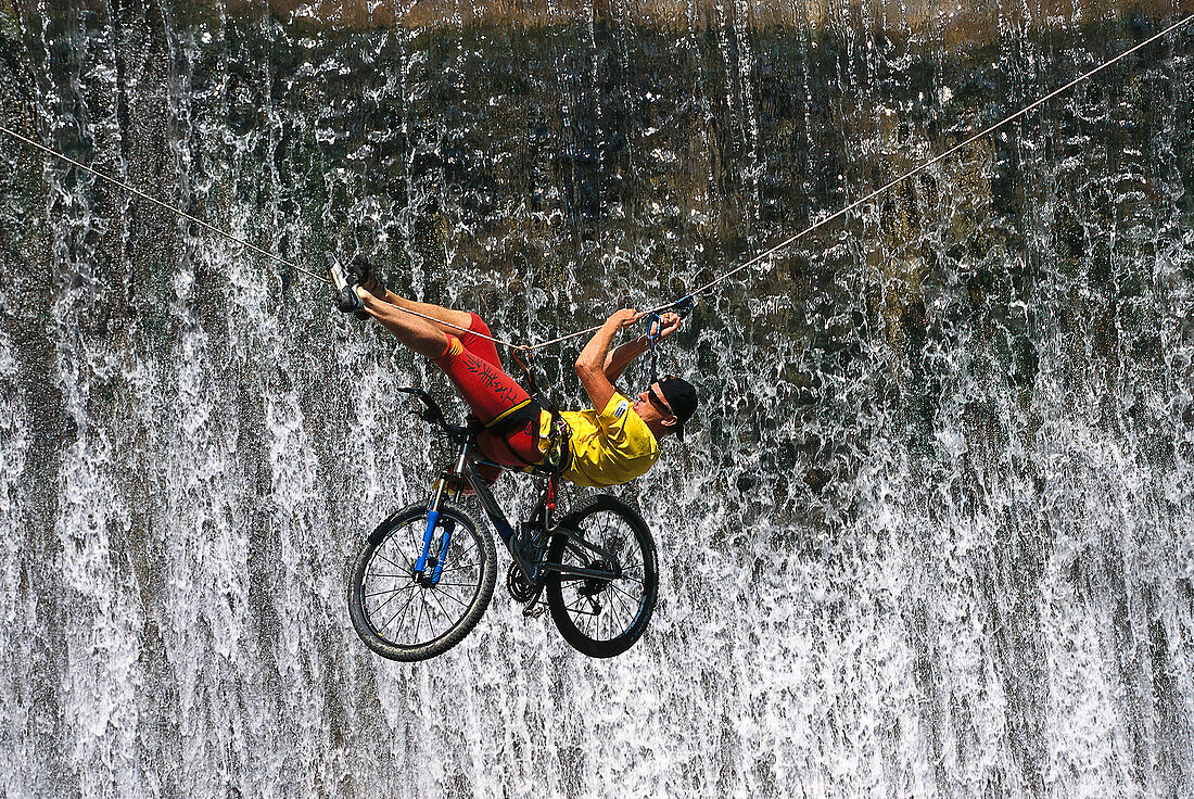 Mountainbiker an einem Seil vor Wasserfall