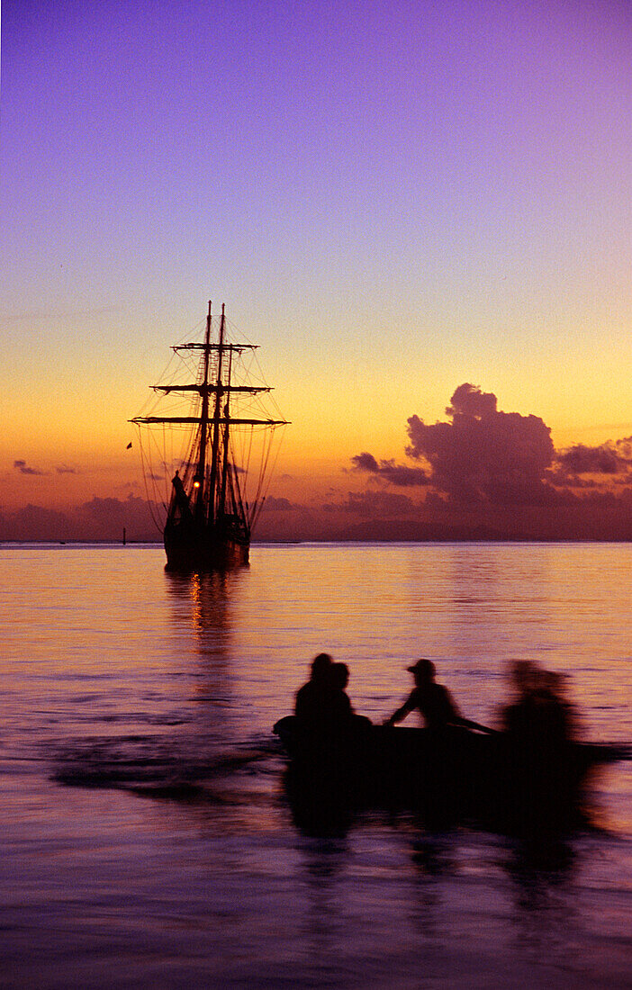 Boat rowing back towards the sailing ship at sunset, Traditional Sailing Ship, Cooks Bay, Moorea, French Polynesia, South Pacific, PR