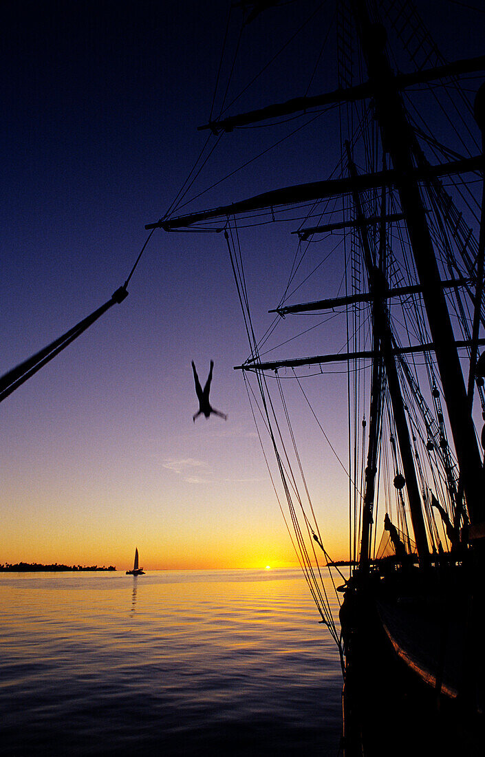 Mann springt bei Sonnenuntergang vom Mast eines Segelschiffs, Bora Bora, Polynesien