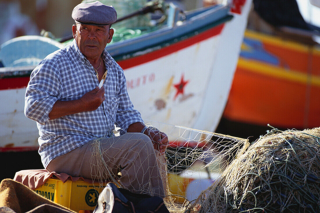 Fisherman repairing a fishing net at harbour, Algarve, Portugal, Europe