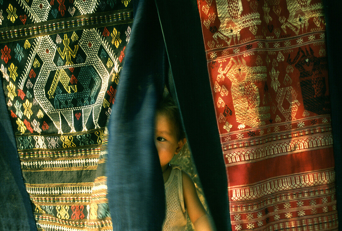 Child hiding behind Lao textiles, Luang Prabang, Laos, Indochina, Asia
