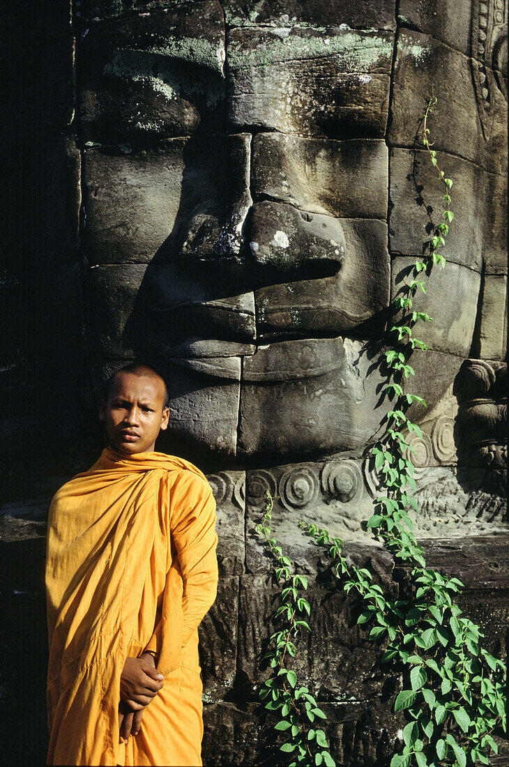 Monk in front of a figure of the Bayon temple, Angkor, Siem Raep, Cambodia, Asia