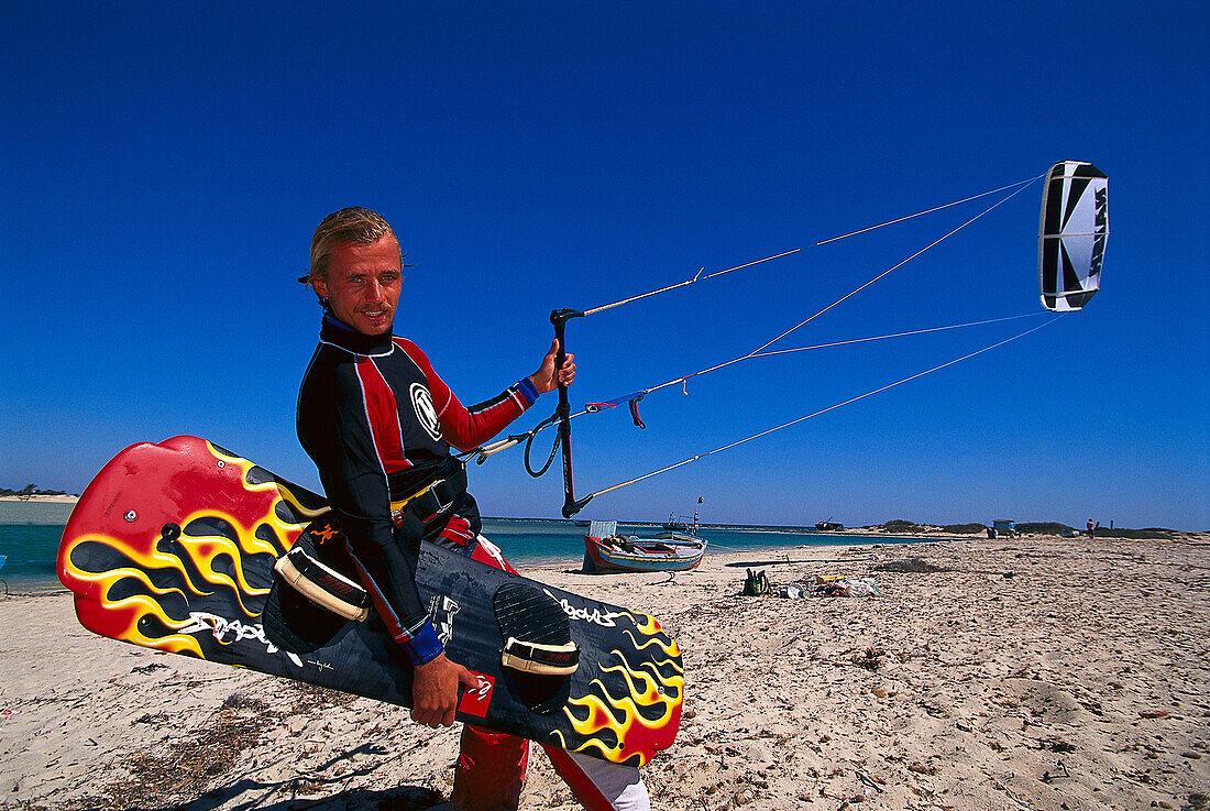 Kitesurfer walking along the beach with his board and kite, Djerba, Tunesia