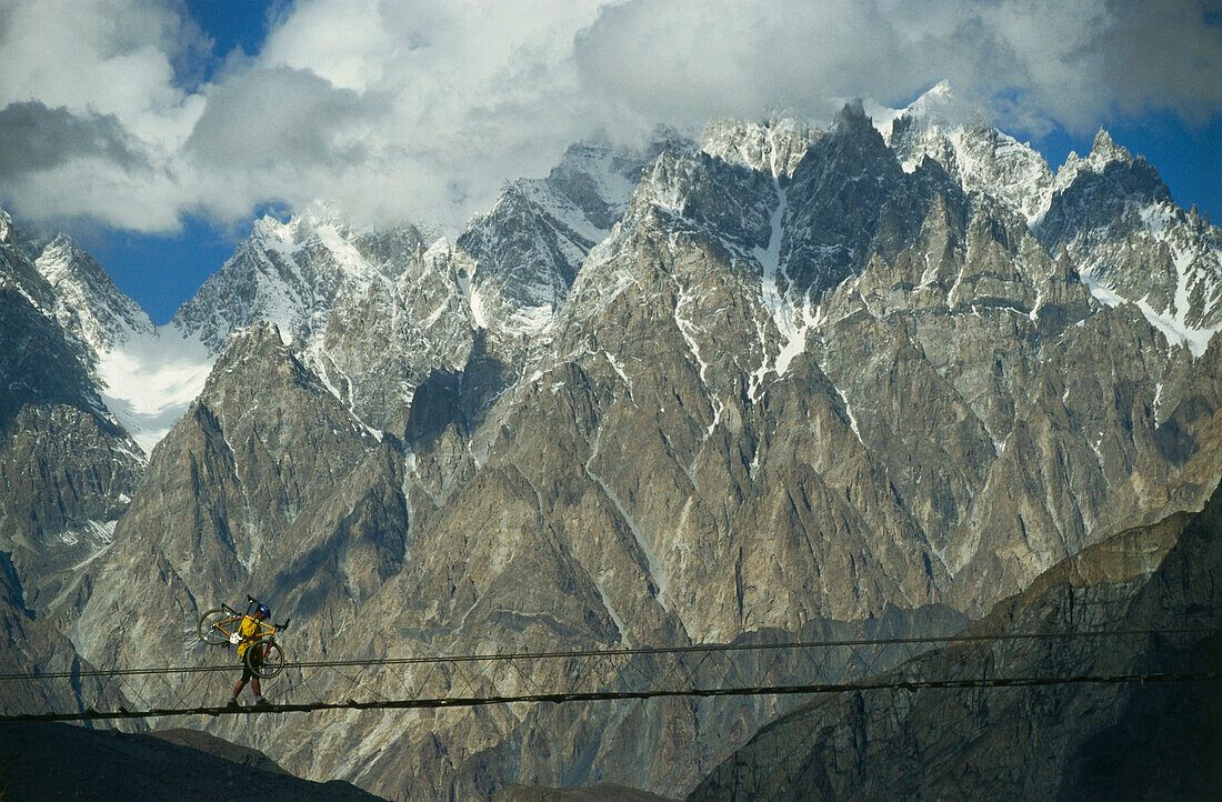 Mountainbiker carrying bike over rope bridge, Karakorum Highway, Pakistan