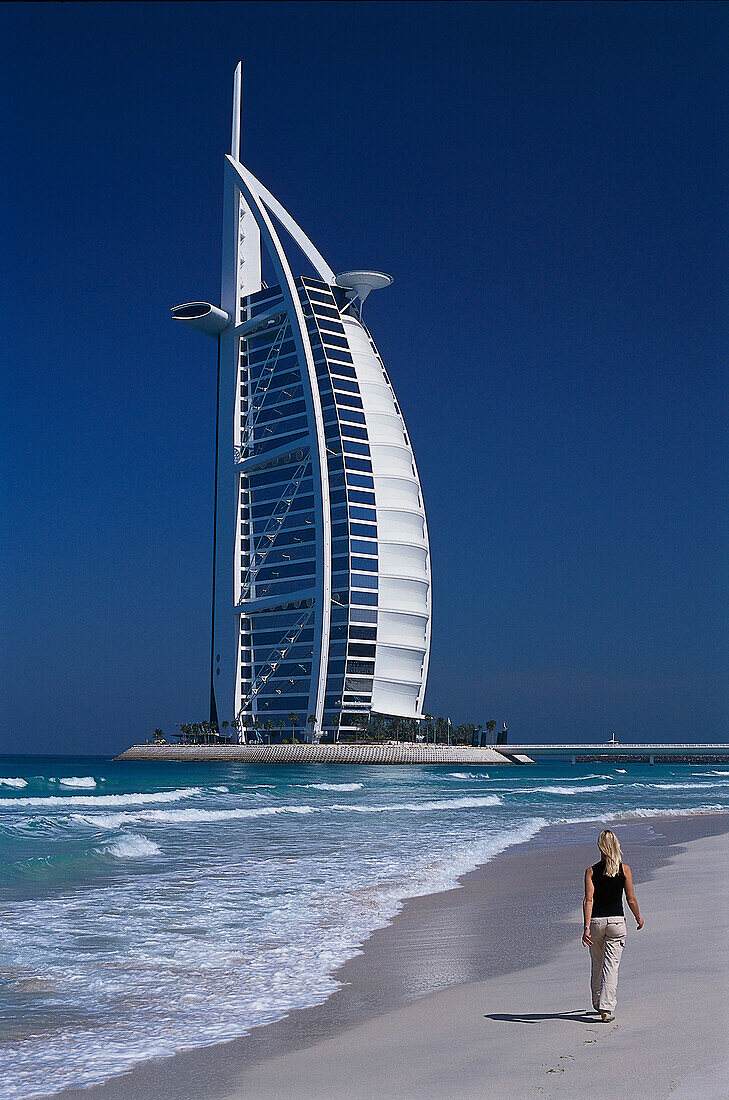 Frau läuft am Strand entlang, Hotel Burj-al-Arab im Hintergrund, Dubai, Vereinigte Arabische Emirate