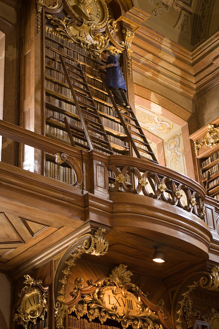 Man sorting books, standing on a ladder, Prunksaal of Nationalbibliothek National Libary, , Vienna, Austria