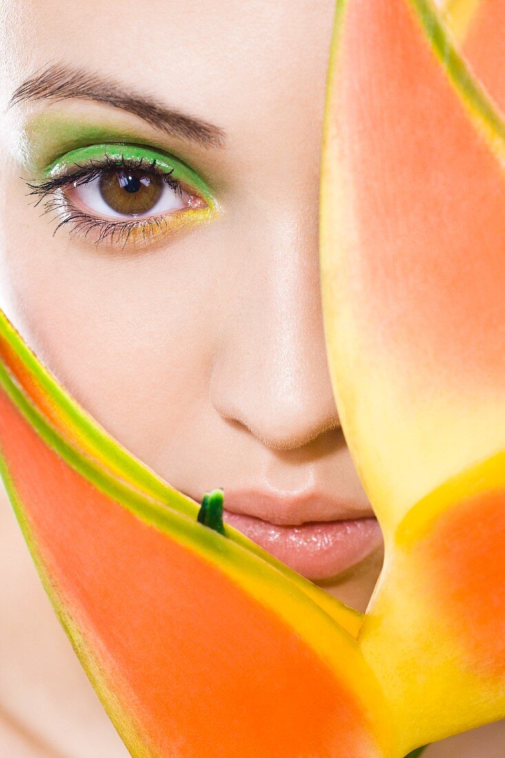 Junge Frau mit grünem Make Up hinter einer Pflanze