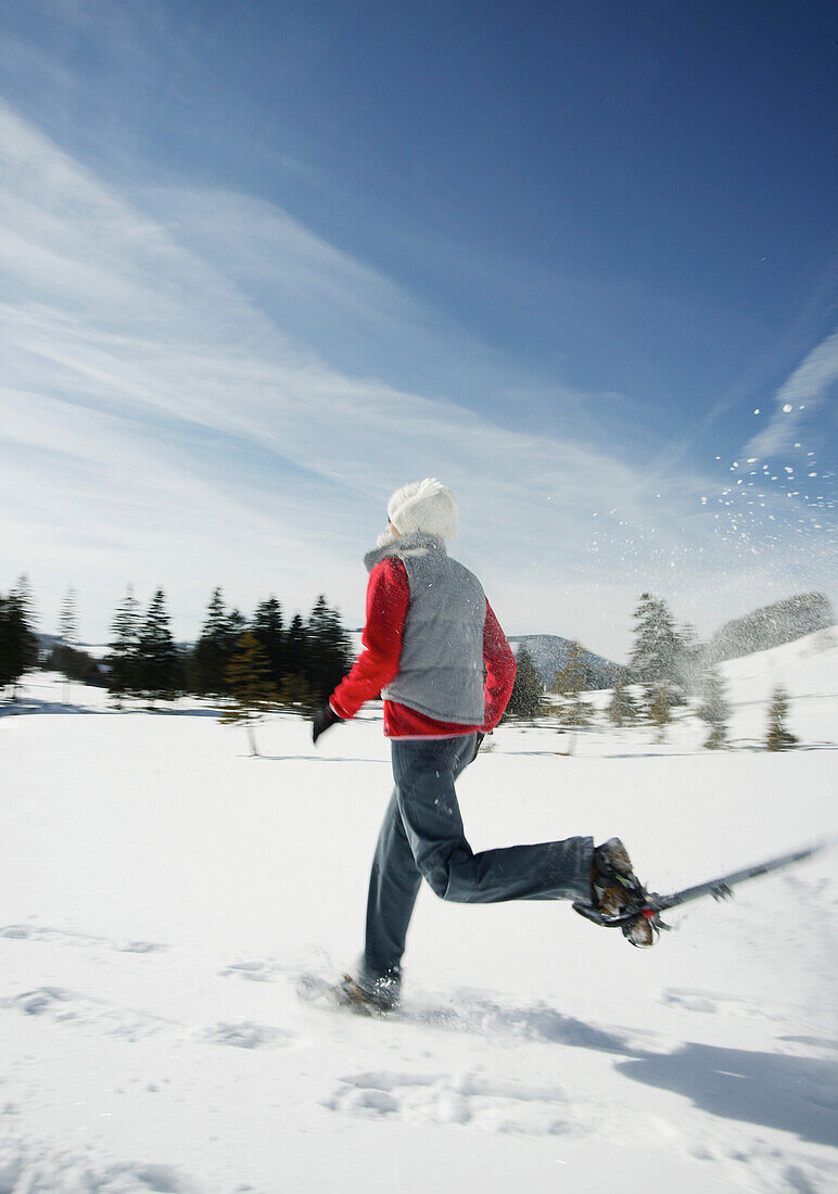 Junge Frau läuft mit Schneeschuhen durch Winterlandschaft