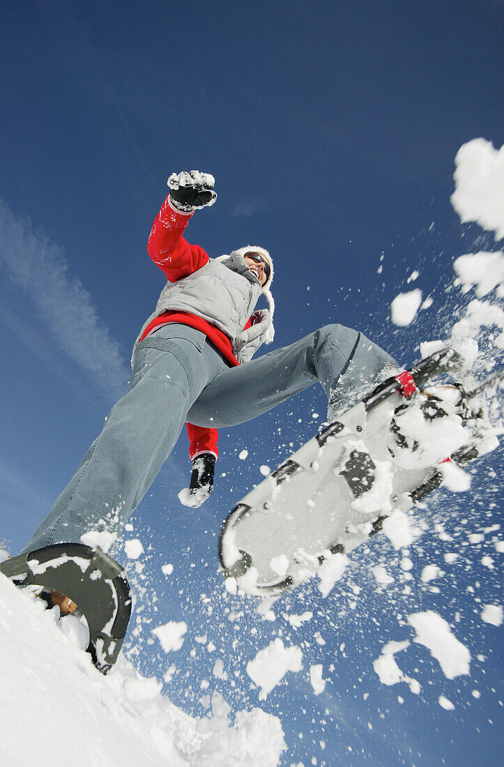 Junge Frau springt mit Schneeschuhen