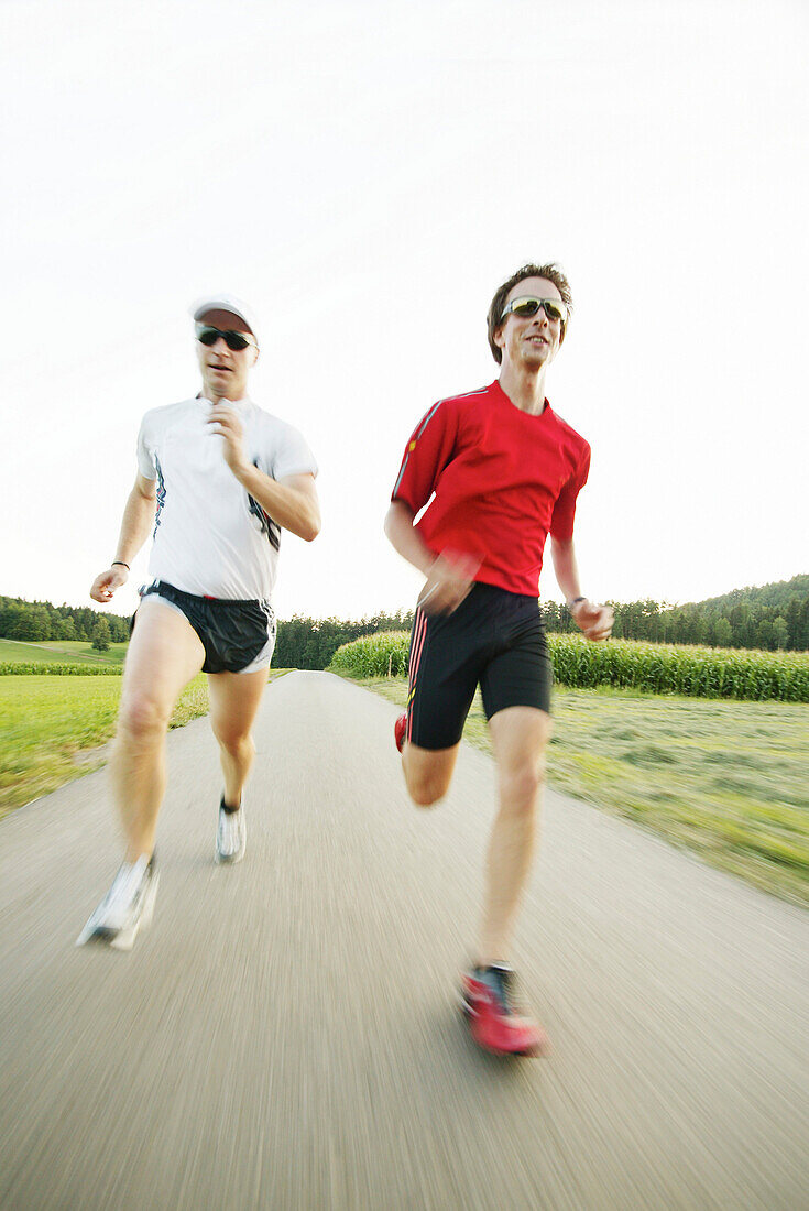 Two young men jogging on country road