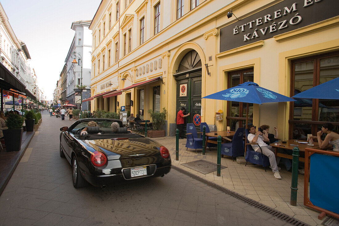Ragtop passing a open-air restaurant , A black ragtop passing a open-air restaurant at Raday Street, Pest, Budapest, Hungary