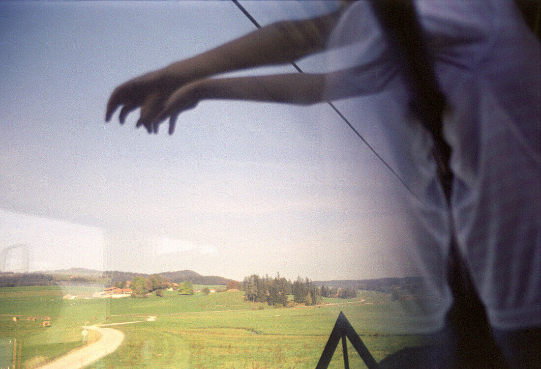 Not recognizeable person reaches out for landscape half reflected in train window, Allgeau, Bavaria, Germany