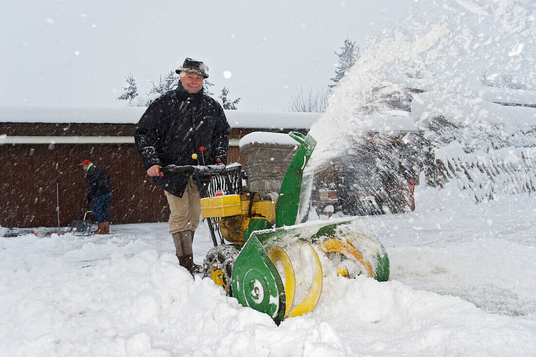 Hauseigentümer beim Schneeräumen mit Schneefräse, Bayern, Deutschland