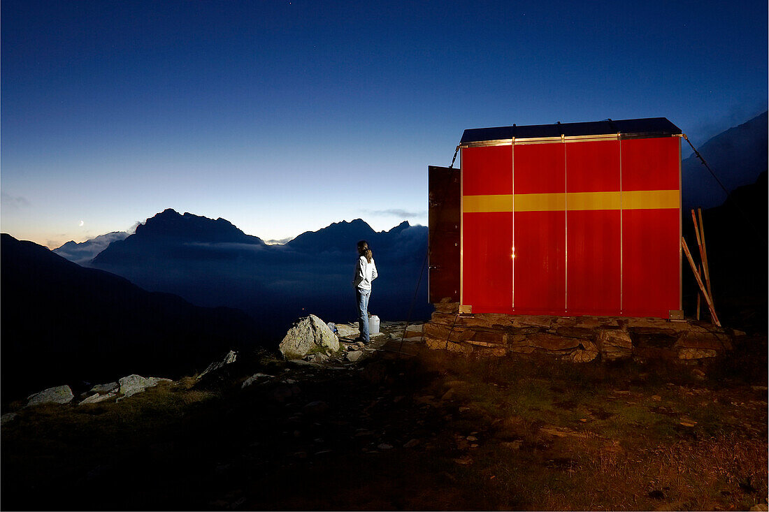 Young woman standing in front of a hut Bivacco Anghileri Rusconi, Passo da Canfinal, Italy