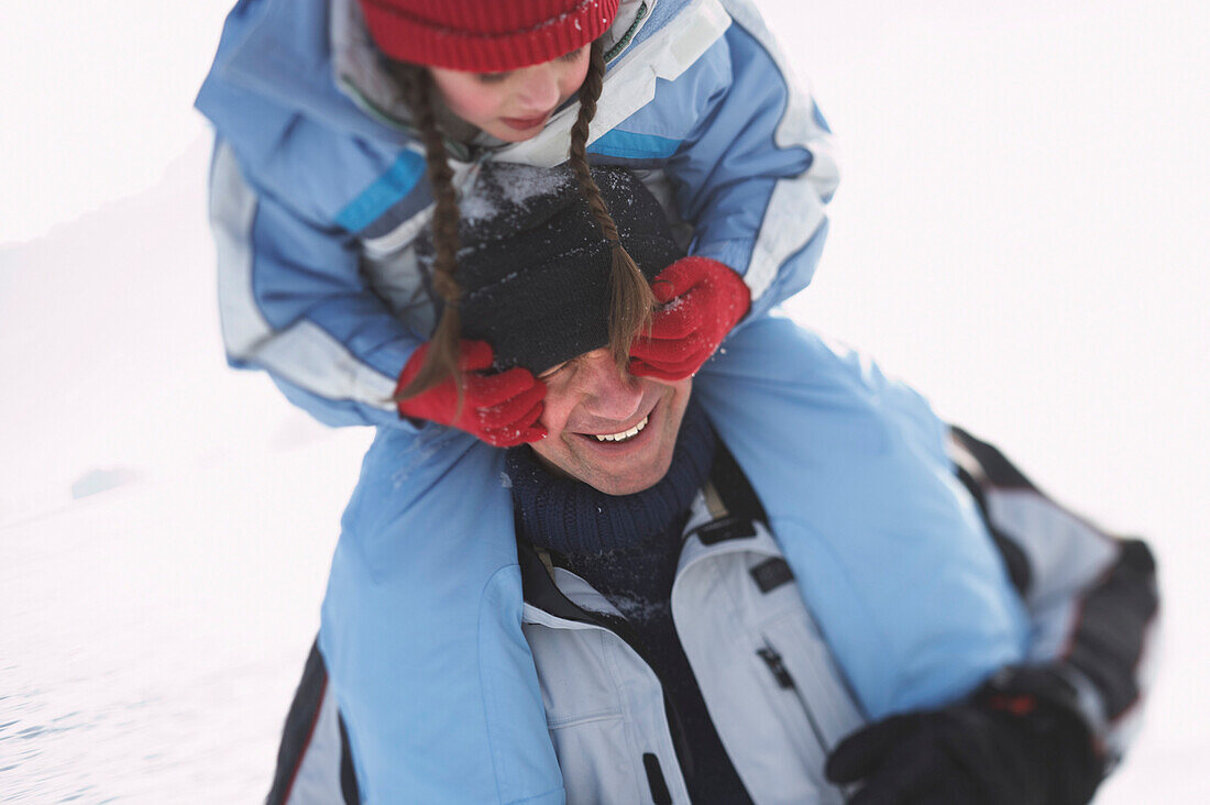 Father carring his daughter on shoulders, girl covering man`s eyes