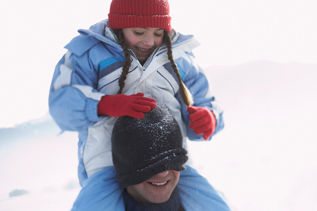 Father carring his daughter on shoulders, pulling knit hat over man´s face