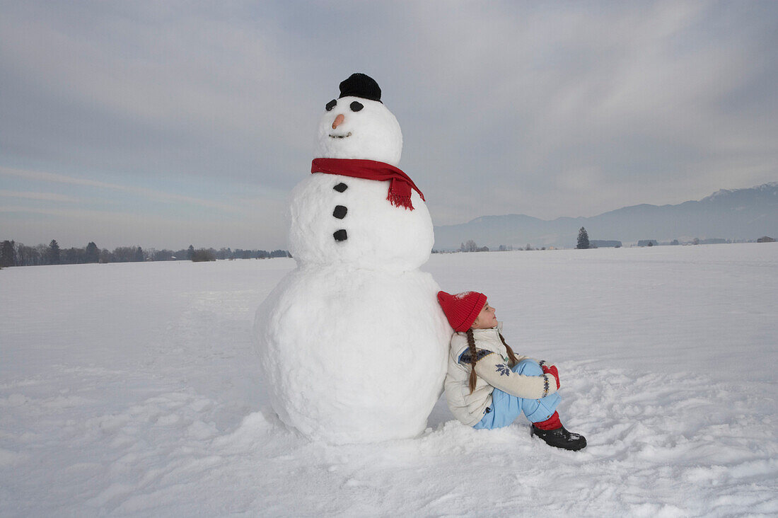 Mädchen 5-6 Jahre, lehnt an einem Schneemann