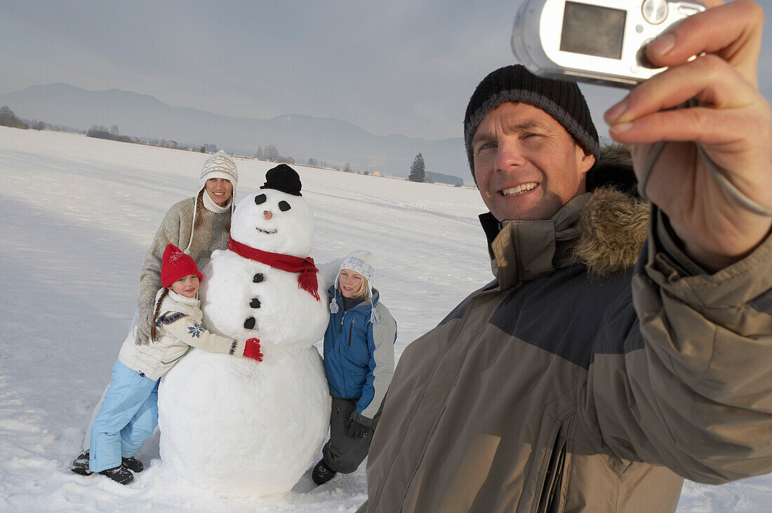 Familie und Schneemann werden vom Vater fotografiert