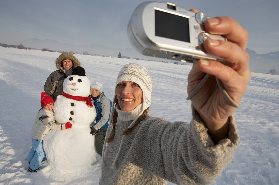 Familie und Schneemann werden von der Mutter fotografiert