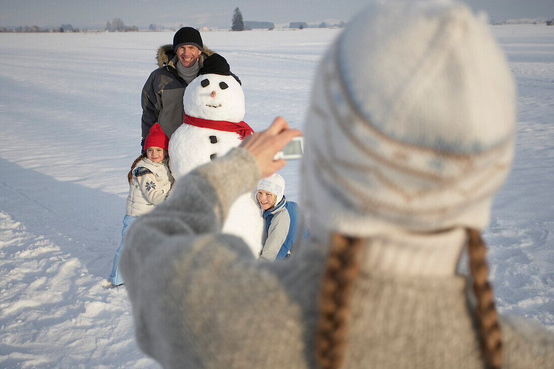 Familie und Schneemann werden von der Mutter fotografiert