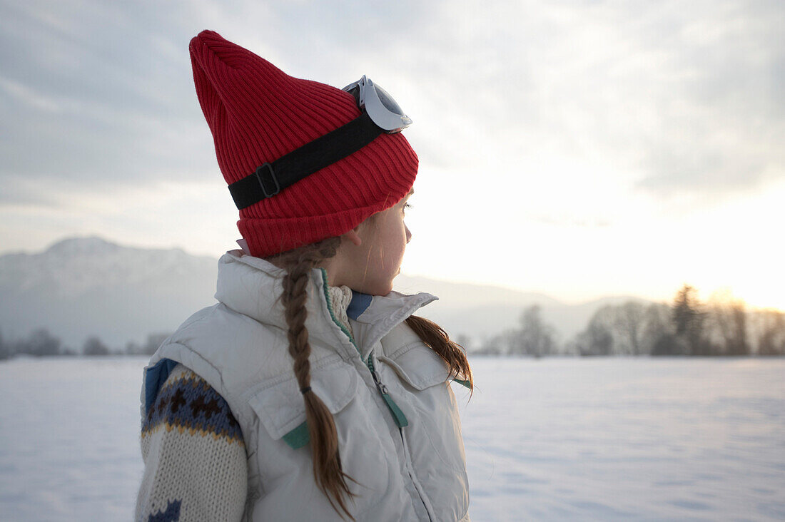 Mädchen 5-6 Jahre, mit roter Wollmütze steht in Winterlandschaft